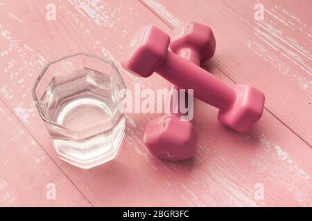 Nahaufnahme der rosa Farbe Hantel und Glas Wasser auf dem Tisch Stockfoto
