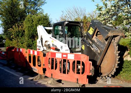 April 2020 - Bobcat-Schlittenlenker-Lader auf Schienen, die mit einem Grabenrad verwendet werden, um Kanäle für Datenkabel im ländlichen Somerset zu verlegen Stockfoto