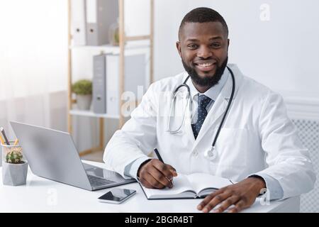 Glücklich schwarzen Arzt Notizen während der Arbeit online Stockfoto