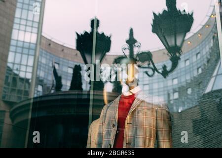 Herrenjacke auf einer Schaufensterpuppe im Schaufenster, mit einem Spiegelbild eines alten Straßenlampenpfosten im Glas Stockfoto