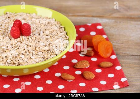 Haferflocken in Schale mit Himbeeren und getrockneten Aprikosen auf einer Serviette mit Polka-Punkt auf Holztisch Stockfoto