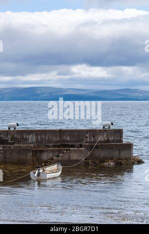 Ruderboot, das an einem Schafspollard auf der Ufermauer im Hafen bei Corrie auf der Isle of Arran, Schottland, festgemacht ist Stockfoto