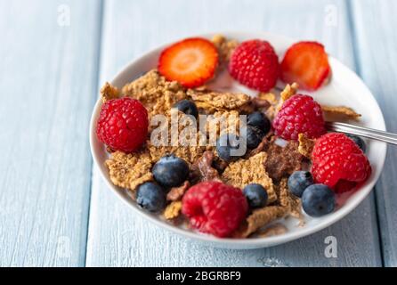 Müsli mit Blaubeeren und Himbeeren in weißer Schale auf dunkelweißem Schreibtisch. Stockfoto