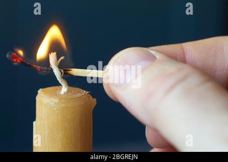 Nahaufnahme männliche Hand hält brennende Spiel und leuchtet gelbe Kerze auf dunklem Hintergrund, selektive Fokus Stockfoto