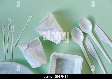 Zwei zertrümmerte weiße Plastikkaffeetassen, Löffel, Messer, Rührer, Teller und Schachtel auf hellgrünem Hintergrund mit Kopierfläche. Konzept ohne Verschwendung. Stockfoto