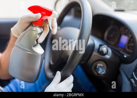 Fahrer trägt Schutzhandschuhe und sprüht Desinfektionsmittel auf das Lenkrad, um Infektionen zu verhindern. Stockfoto