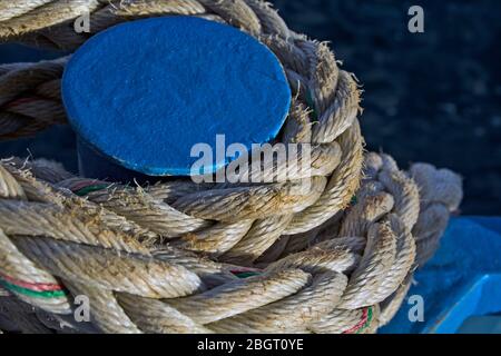 Das Seil, das das Boot an den blauen Metallmast am Ufer der Marina festgebunden hat. Stockfoto