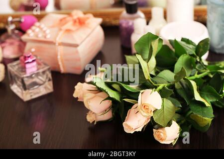 Schöne Rosen, Parfüms auf dem Tisch in der Nähe des Spiegels Stockfoto