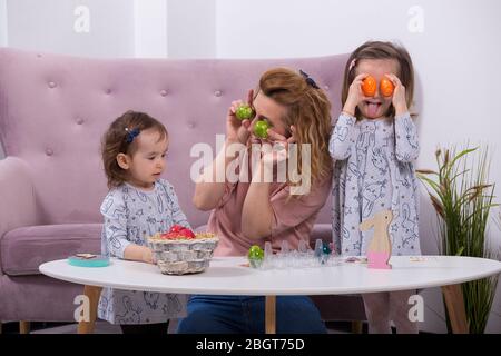 Mutter und Töchter malen Eier. Glückliche Familie bereitet sich auf Ostern vor. Quarantäne zu Hause. Stockfoto