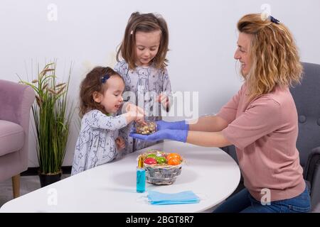 Mutter und Töchter feiern Ostern, essen Schokoladeneier. Frohes Familienfest. Nette kleine Mädchen lachen, lächeln und Spaß haben. Stockfoto