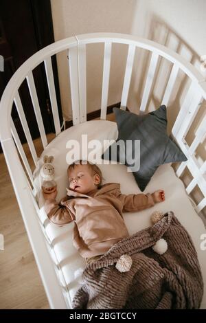 Niedliches kleines 1-jähriges Baby liegt auf einem Kinderbett, während es mit Lichtfenstern im Gesicht schläft, Tagesschlaf-Konzept Stockfoto