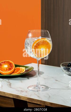 Gin Tonic Cocktail, garniert mit orangefarbenen Scheiben, farbenfroher Hintergrund Stockfoto