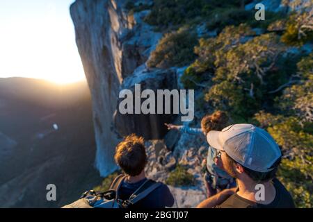 Drei Wanderer, die bei Sonnenuntergang die Nase El Capitan von oben betrachten Stockfoto