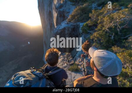 Drei Wanderer, die bei Sonnenuntergang die Nase El Capitan von oben betrachten Stockfoto