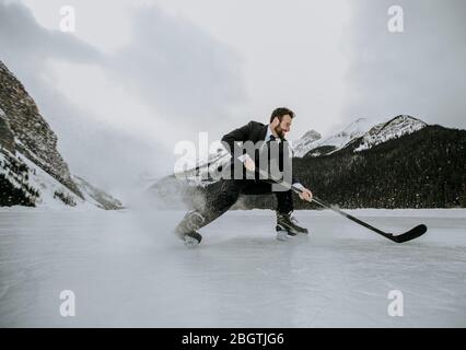 Hockeyspieler auf gefrorenem See im Anzug stoppt schnell und spritzt Eis Stockfoto