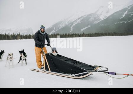 Mann und Frau Paar sitzen und stehen in Hundeschlitzen in kanadischen rockies Stockfoto