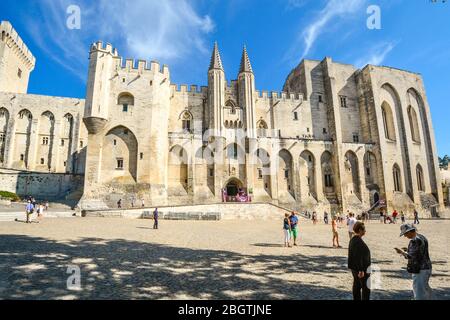 Touristen mischen sich auf dem Platz vor dem Papstpalast, einem riesigen mittelalterlichen Schloss und einer Festung in Avignon in der Provence Stockfoto