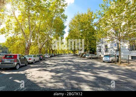 Autos werden entlang einer von Bäumen gesäumten Straße in einem gehobenen Viertel geparkt, das entlang des Tiber Flusses in Rom, Italien läuft. Stockfoto