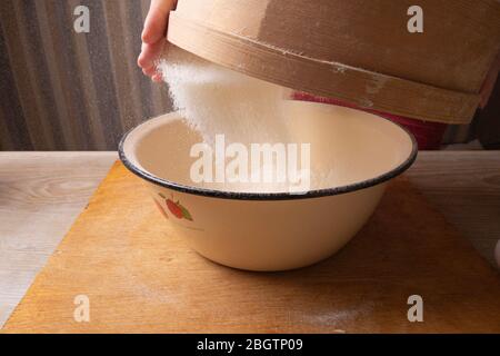 Große Schüssel, Schneidebrett, Sieb zum Sieben von Mehl auf dem Tisch. Weibliche Hände sieben Mehl in der Küche. Stockfoto