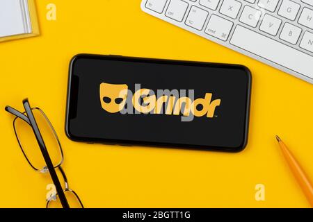 Ein Smartphone mit Grindr-Logo liegt auf gelbem Hintergrund zusammen mit Tastatur, Brille, Stift und Buch (nur für redaktionelle Verwendung). Stockfoto