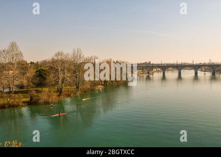 Erhöhte Ansicht des Flusses Mincio mit drei Mann Kanufahren und die Bogenbahn Brücke im Hintergrund, Peschiera del Garda, Verona, Veneto, Italien Stockfoto