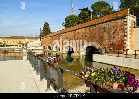 Blick auf die Ponte dei Voltoni Bogenbrücke (16. jh.) über den Mittleren Kanal, der die Altstadt von Peschiera del Garda, Verona, Venetien, Italien überquerte Stockfoto