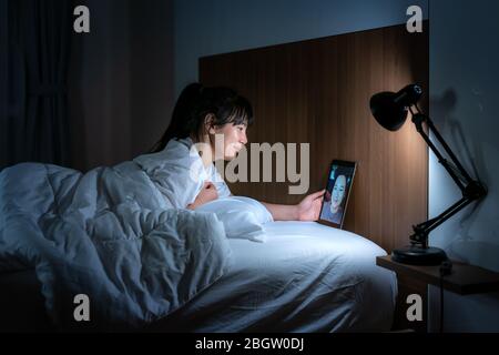 Asiatische Frau virtuelle Happy Hour Treffen online zusammen mit ihrem Freund in Videokonferenz gute Nacht vor dem Schlaf in der Nacht mit digitalen Tablet Stockfoto