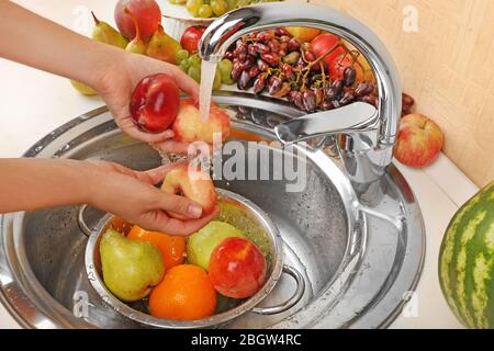 Frauenhände waschen Pfirsiche und andere Früchte in Sieb im Waschbecken Stockfoto