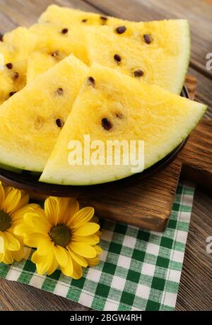 Scheiben Wassermelone auf Teller auf Schneidebrett auf karierter Serviette und gelbe Blumen auf Holzhintergrund Stockfoto