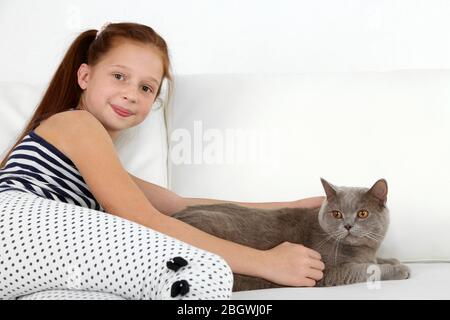 Schönes kleines Mädchen mit Katze auf dem Sofa im Zimmer Stockfoto