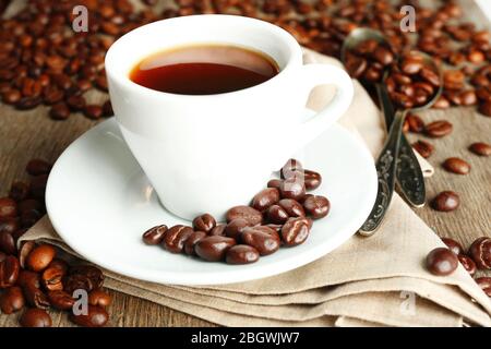 Tasse Kaffee und Kaffeebohnen mit Schokoladenglasur auf Holzhintergrund Stockfoto