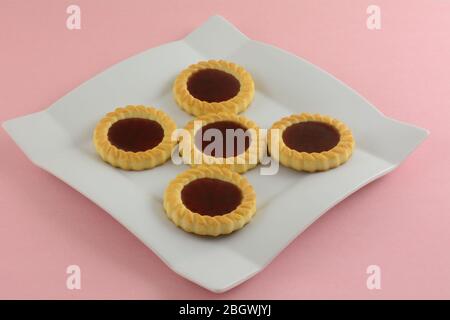 Nahaufnahme von roten Himbeer-Frucht-Tartlette-Cookies auf weißem Dessertteller auf rosa Hintergrund Stockfoto