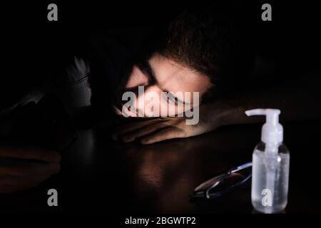 Ein Arzt erschöpft ruhend auf dem Tisch in der Nacht mit dem Handy-Bildschirm Beleuchtung, der Kinnriemen und der Gel-Alkohol während der covid 19 Pandemie Stockfoto