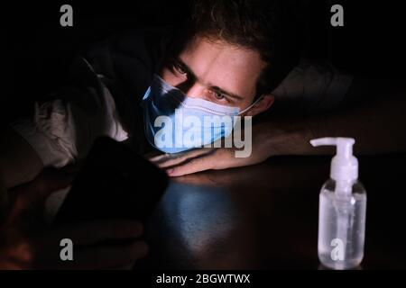 Ein Arzt erschöpft ruhend auf dem Tisch in der Nacht mit dem Handy-Bildschirm Beleuchtung, der Kinnriemen und der Gel-Alkohol während der covid 19 Pandemie Stockfoto