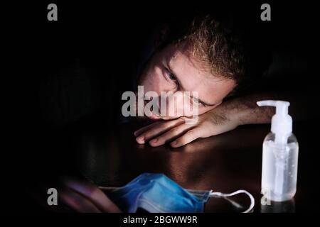 Ein Arzt erschöpft ruhend auf dem Tisch in der Nacht mit dem Handy-Bildschirm Beleuchtung, der Kinnriemen und der Gel-Alkohol während der covid 19 Pandemie Stockfoto