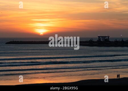 Sonnenuntergang am Strand in Essaouira Marokko in der Nähe des Horizonts mit Wellen und der Werft Stockfoto