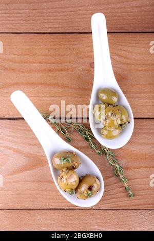 Grüne Oliven in Öl mit Gewürzen und Rosmarin in Löffeln auf Holztisch Stockfoto