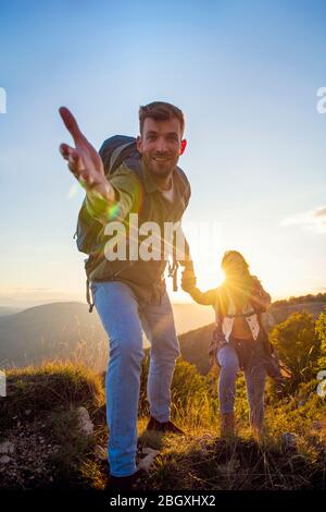 Menschen helfen sich gegenseitig, bei Sonnenaufgang einen Berg hinauf zu wandern. Stockfoto