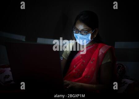 Junge inderin mit Maske, die spät abends auf ihrem Laptop arbeitet, Freiberufler, die von zu Hause aus arbeitet. Coronavirus, Covid-19. Bleiben Sie zu Hause bleiben Sie sicher, Frau in qu Stockfoto