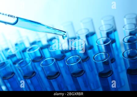 Pipette, die blaue Flüssigkeit auf das Reagenzglas auf hellem Hintergrund aufgibt Stockfoto