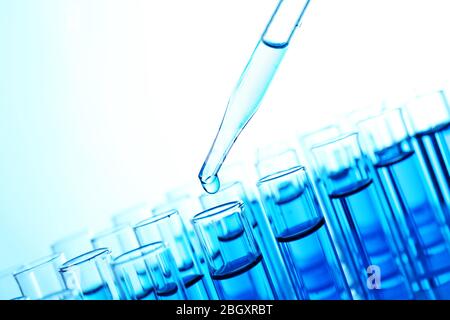 Pipette, die blaue Flüssigkeit auf das Reagenzglas auf hellem Hintergrund aufgibt Stockfoto