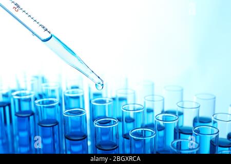 Pipette, die blaue Flüssigkeit auf das Reagenzglas auf hellem Hintergrund aufgibt Stockfoto