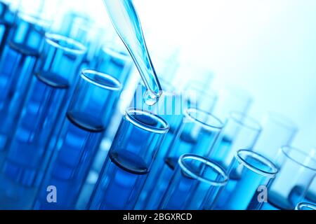 Pipette, die blaue Flüssigkeit auf das Reagenzglas auf hellem Hintergrund aufgibt Stockfoto