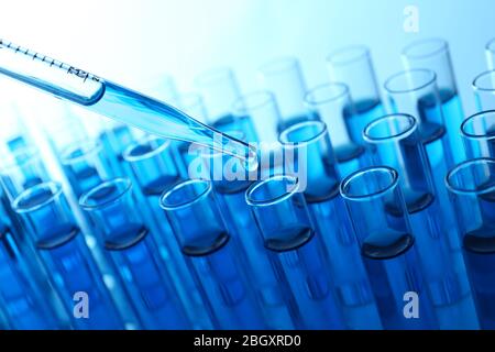 Pipette, die blaue Flüssigkeit auf das Reagenzglas auf hellem Hintergrund aufgibt Stockfoto