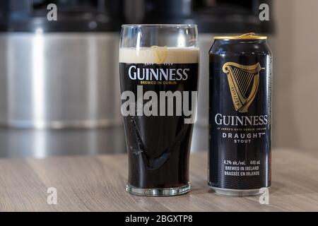 Guinness-Bierfass kann auf einem Tisch neben einem vollen Glas Bier in einem Guinness-Glas mit gestapelten Fässern im Hintergrund schreien. Stockfoto
