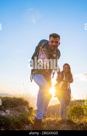 Menschen helfen sich gegenseitig, bei Sonnenaufgang einen Berg hinauf zu wandern. Stockfoto