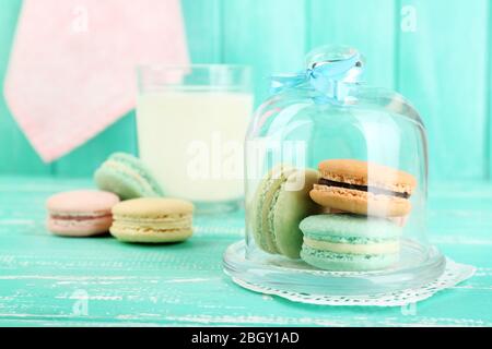 Sanfte bunte Makronen in Glas Bell jar, Milch Glas und Handtuch auf Farbe holztisch Hintergrund Stockfoto