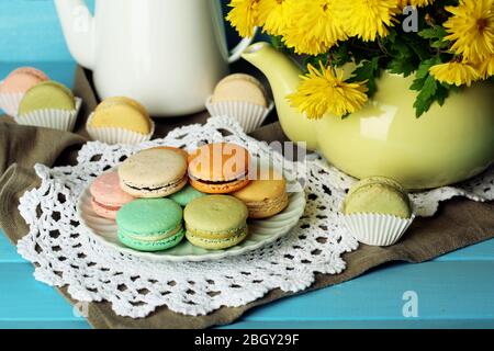 Zusammensetzung der gelben Blüten in dekorativer Teekanne, Tasse mit Heißgetränk und leckeren Makronen auf Holzhintergrund Stockfoto