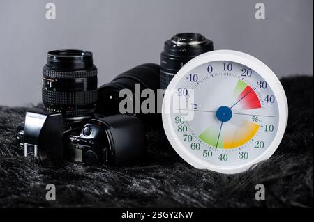 Weißes analoges Thermometer und Hygrometer mit Fotoausrüstung. Objektive und Kameraausrüstung werden optimal bei einer relativen Luftfeuchtigkeit (RH) eines gelagert Stockfoto