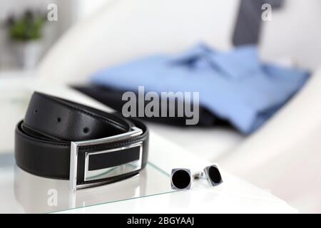 Herrengürtel und Manschettenknöpfe auf Kaffeetabellemit Hemd und Krawatte auf Stuhl auf Hintergrund Stockfoto